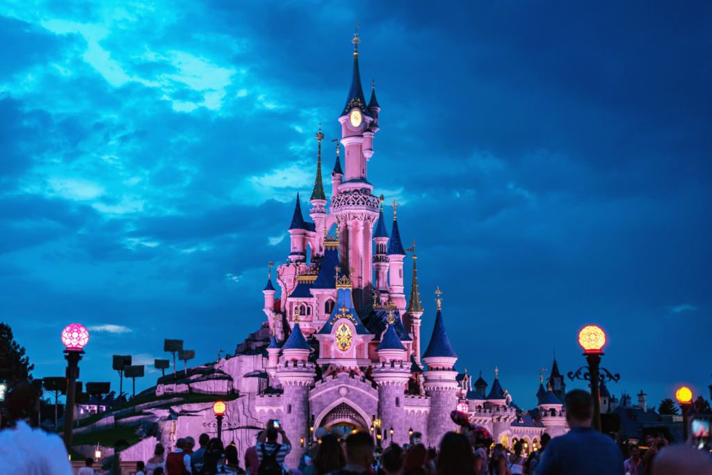 Enchanting castle at dusk with vibrant lights, surrounded by visitors under a dramatic blue sky.